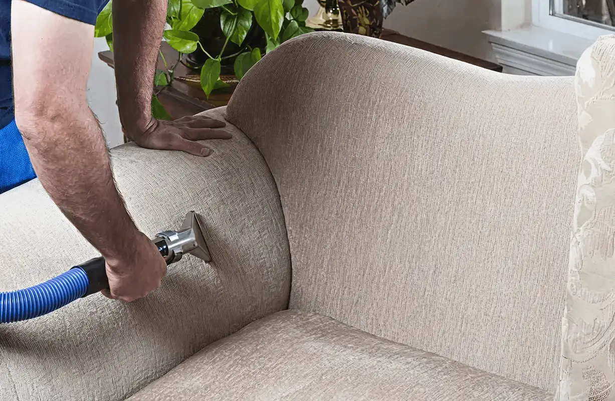Professional upholstery cleaner deep-cleaning a fabric sofa with a handheld extraction tool and hose, Overland Park, KS.